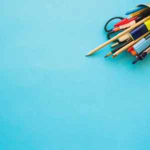 Photo de fournitures de bureau vendues à la Papeterie Valles à Lourdes (65100) dans les Hautes-Pyrénées. Un pot à crayon renversé avec des stylos, des crayons, un compas, un surligneur, des ciseaux et un pinceau.